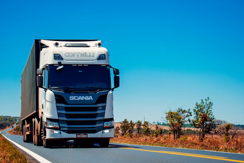 White Scania freight truck on an open highway under a clear sky.